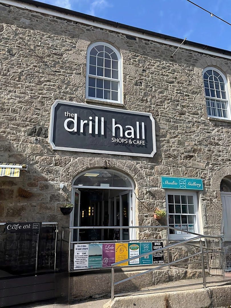 The Drill Hall on Chapel Street: a granite front with arched windows, an arched doorway and a black sign reading 'the drill hall, shops & cafe'