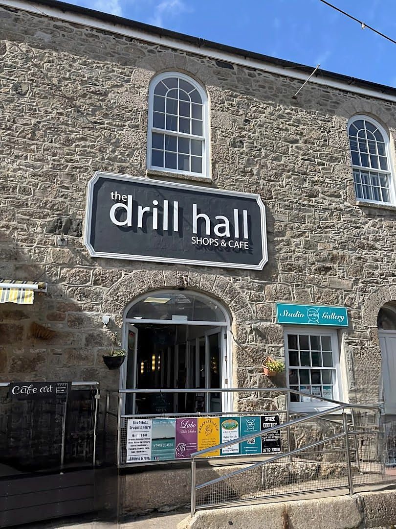 The Drill Hall on Chapel Street: a granite front with arched windows, an arched doorway and a black sign reading 'the drill hall, shops & cafe'