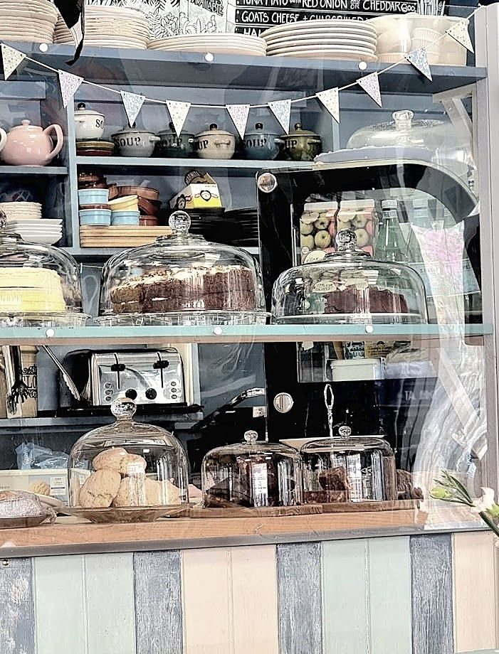 The counter: cakes under glass domes on blue shelves, teapots and bunting above