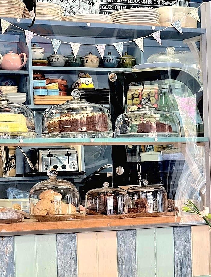 The counter: cakes under glass domes on blue shelves, teapots and bunting above