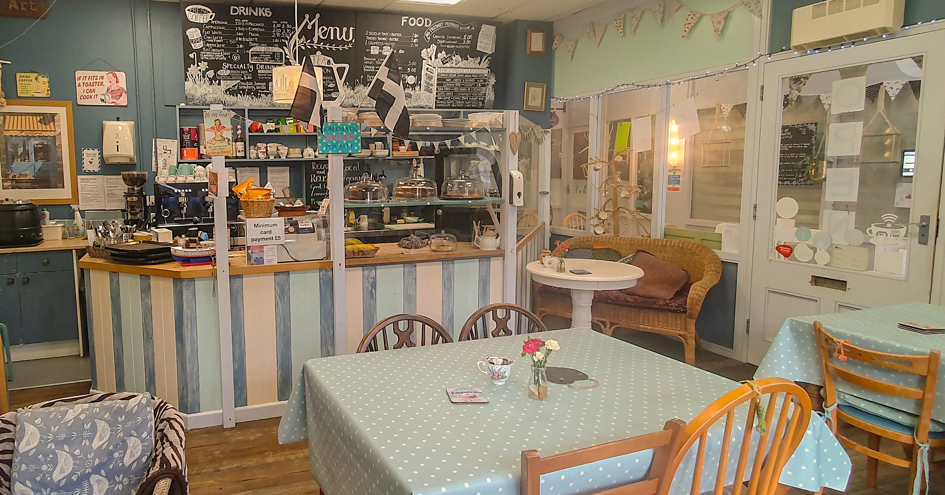 Inside Cafe Art: duck-egg blue walls, a hand-drawn chalkboard menu, two black-and-white Cornish flags, bunting and spotted oilcloth on the tables