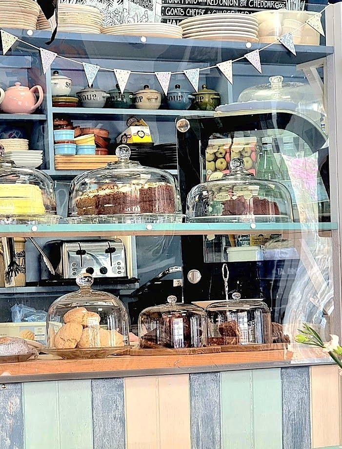 The counter: cakes under glass domes on blue shelves, teapots and bunting above