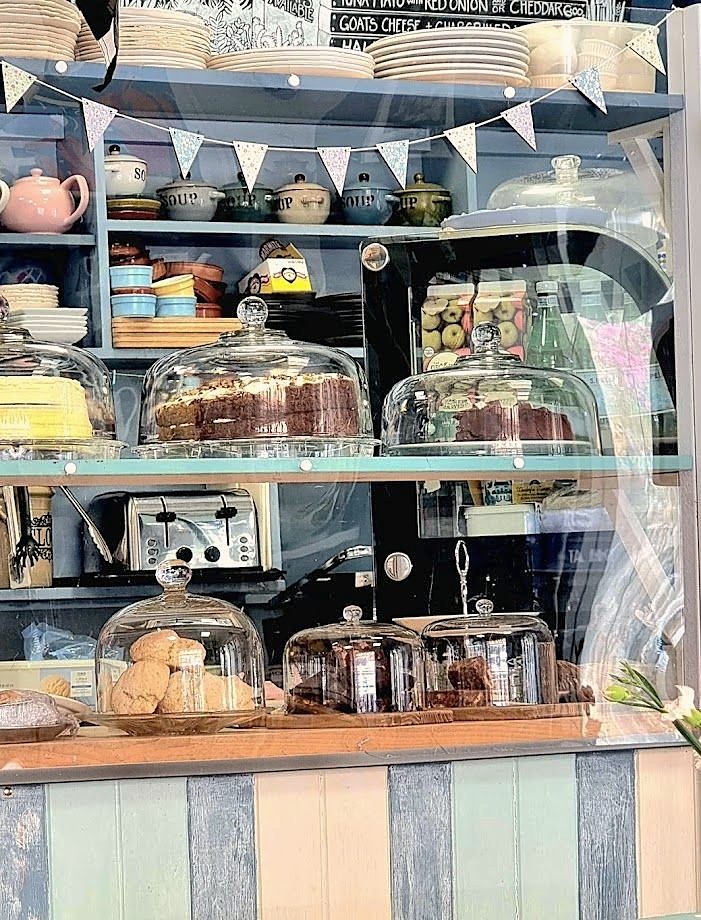 The counter: cakes under glass domes on blue shelves, teapots and bunting above